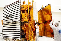 Photo montrant des techniciens en train de fixer les panneaux solaires sur le corps de la sonde spatiale
