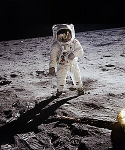 Un astronaute regarde la caméra, le sol est désertique autour.