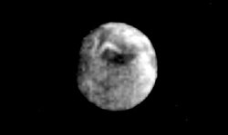 La lune Miranda vue entière et ronde par la sonde Voyager 2. Sa surface grise permet d'apercevoir le chevron blanc d'Inverness corona.