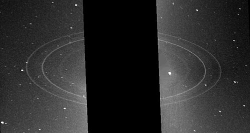 Image éloignée de la planète, trois grands anneaux sont visibles et la planète cachée par une bande noire.