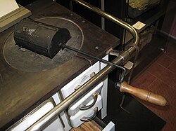 demi-cylindre muni d'une longue manivelle, posé par son long côté plat sur une plaque métallique qui ferme le trou à marmite du fourneau.