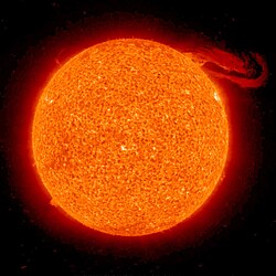 Vue du Soleil de couleur orangée. Une grande traînée s'en échappe sur la droite.