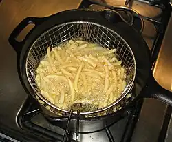 Frites dorant dans un panier grillagé plongé dans l’huile d’une casserole en fonte posée sur une gazinière