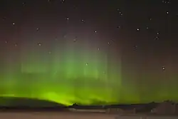 Une lueur ondoyante dans le ciel nocturne au-dessus du sol couvert de neige.
