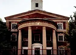 Façade de l'école en brique rouge, avec des colonnes et encadrements de fenêtres blancs.