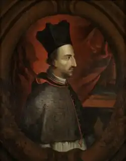 Huile sur toile, couleurs dominantes marron et noir, portrait d’un homme de face, portant une coiffe et revêtu d'un manteau bordé de fourrure ; sa main droite est posée sur un livre ouvert où figure son nom